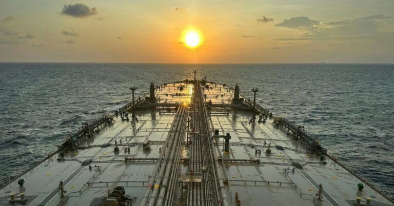 View across the deck of a crude oil tanker traveling at sea at sunset.