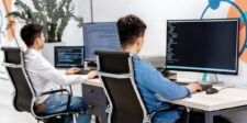 Software developers reviewing code across multiple computer screens in an office.