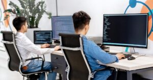 Software developers reviewing code across multiple computer screens in an office.