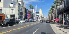 Hollywood Boulevard in Los Angeles with theaters, palm trees, traffic, and pedestrians.