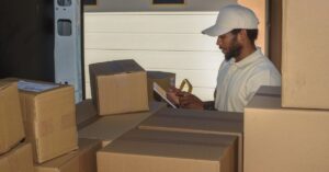 Delivery worker checking packages beside a van loaded with cardboard parcels.