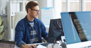 Web developer working at a desk with multiple monitors displaying code.