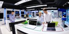 AI is starting to raise the price of everyday electronics Shoppers comparing laptops and other electronics in a retail store, illustrating rising consumer technology costs.