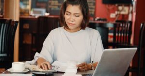 Small-business owner reviewing receipts and expenses with a calculator and laptop, illustrating the cost of competing with AI tools.