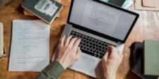 Apple says Safari now blocks identity resolution infrastructure Overhead view of a person typing on a MacBook Pro at a wooden table with books and papers.
