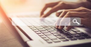 Hands typing on a laptop with a search-bar graphic across the image.