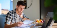 Atlassian raises Jira and Confluence Cloud prices on Oct. 13 Concerned man reviewing bills and expenses beside a laptop, illustrating rising Jira and Confluence Cloud prices.