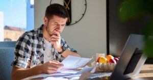 Concerned man reviewing bills and expenses beside a laptop, illustrating rising Jira and Confluence Cloud prices.