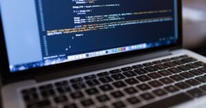 MacBook displaying code on a dark screen above its keyboard.
