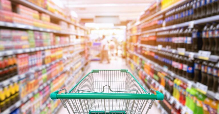 Shopping cart in a supermarket aisle lined with stocked shelves.