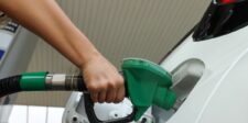 Hand holding a green fuel nozzle while filling up a white car