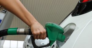 Hand holding a green fuel nozzle while filling up a white car