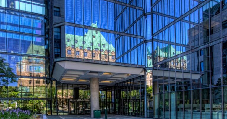 Bank of Canada entrance in Ottawa with historic buildings reflected in its glass facade.