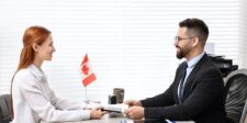 Job candidate and interviewer passing a document across a desk with a small Canadian flag