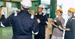 Supervisor in a hard hat leading a training session with factory workers