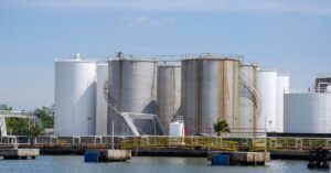 Large petroleum storage tanks at a waterfront fuel terminal, illustrating diesel supply and reserve-release pressures.