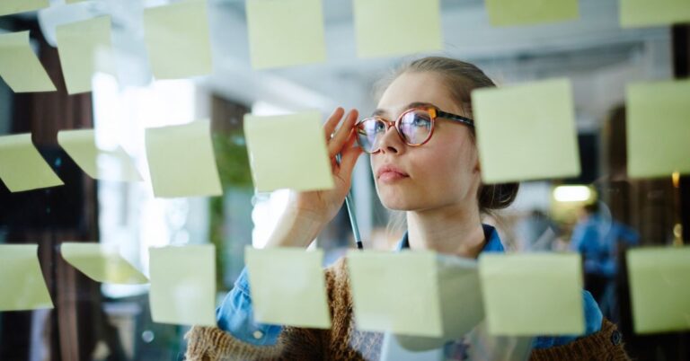 Entrepreneur planning business growth with sticky notes on a glass wall.