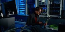 IT administrator working on a laptop beside server racks and network equipment.