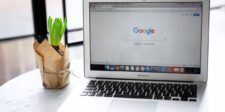 MacBook Air displaying the Google Search homepage beside a potted plant.