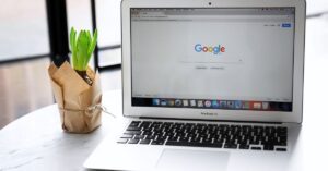 MacBook Air displaying the Google Search homepage beside a potted plant.