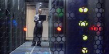 Google Cloud outage disrupts UK banks and public services after London power event Technician with a laptop standing in a dim data center aisle between server racks with glowing status lights