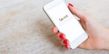 Hand with red nails holding a white smartphone displaying a search page.