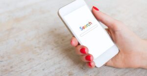 Hand with red nails holding a white smartphone displaying a search page.