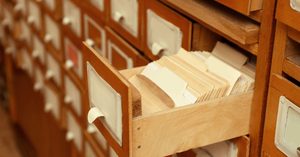 An open wooden library card catalog drawer packed with index cards