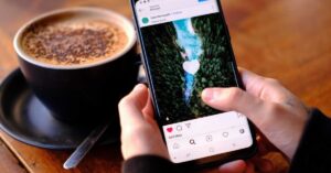 Hands holding a phone displaying Instagram beside a cup of coffee
