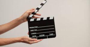 Hands holding an open black-and-white film clapperboard against a beige background.