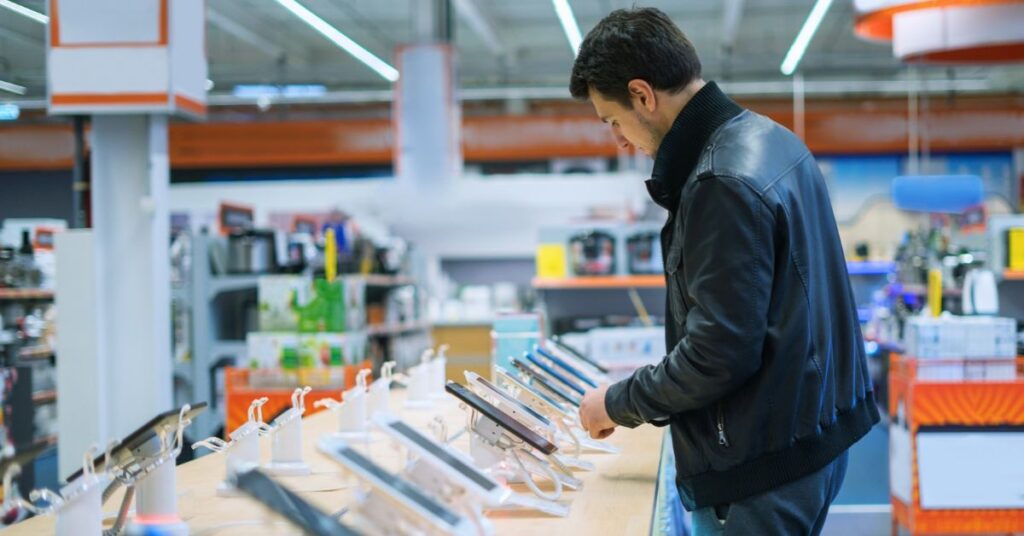 Customer examining smartphones in an electronics store, illustrating low-cost Android phones found with preinstalled firmware malware.