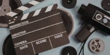 Film clapperboard, vintage movie camera and film reels on a blue-gray surface.