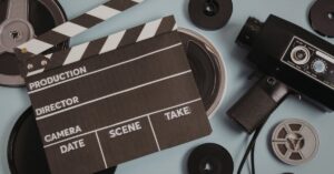 Film clapperboard, vintage movie camera and film reels on a blue-gray surface.