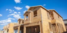 Ontario municipalities cut residential development charges under infrastructure funding deals Wood-frame houses under construction beneath a blue sky.