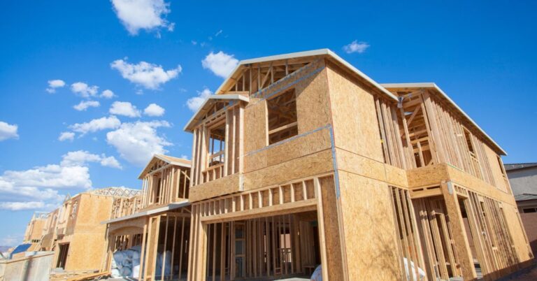 Wood-frame houses under construction beneath a blue sky.