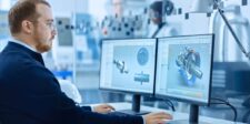 Engineer using CAD software to review industrial component designs on dual monitors in a manufacturing environment.
