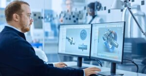 Engineer using CAD software to review industrial component designs on dual monitors in a manufacturing environment.
