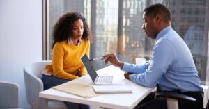Business owner meeting with an advisor and reviewing information on a laptop while preparing for a potential business sale.