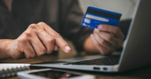 Person holding a blue credit card while typing on a laptop