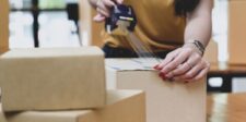 Shopify adds guaranteed flat-rate shipping to Managed Markets A person seals a cardboard shipping box with packing tape beside other parcels.