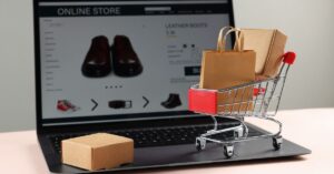 Mini shopping cart with paper bags and a parcel on a laptop displaying an online store.