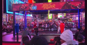 Live performers dressed as Ryu and Ken fighting inside a giant Street Fighter arcade cabinet in Times Square.