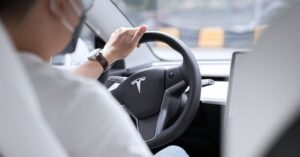 Driver holding the steering wheel inside a Tesla, illustrating the company’s shift from Full Self-Driving branding to Assisted Driving in Europe.