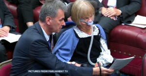 Member of the House of Lords using an assistive breathing device during a speech delivered with an AI-generated recreation of her voice.