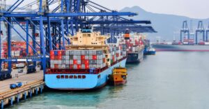 Container ships loaded with cargo at a major port, illustrating strong U.S.-bound freight demand and elevated shipping costs.